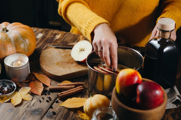 Фото Взгляд сверху женщины в желтом свитере кладя cutted яблоки в бак для делать горячее вино.