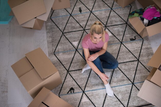Фото Вид сверху на молодую красивую женщину, сидящую и отдыхающую на полу после переезда в новый дом с картонными коробками вокруг нее