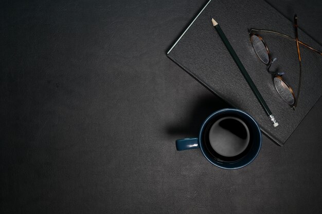 Top view office dark desk table workplace with coffee and supplies. 