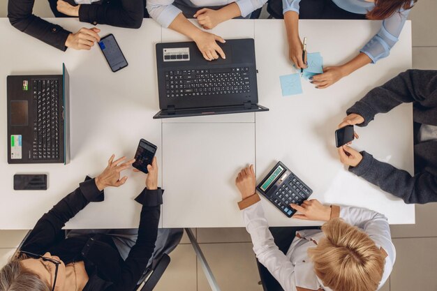 Top view of the office desk. Group of concentrated workers holding phones, laptops, and calculators in their hands. Successful concept. Productivity atmosphere