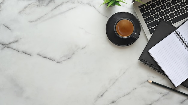 Top view office desk marble table with  laptop, notebook paper, pencil and espresso coffee.