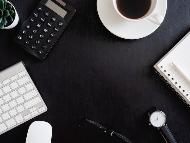 Photo top view of office desk table with notebook, plastic plant, calculator and keyboard on black background, graphic designer, creative designer concept.