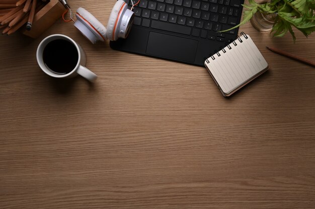 Top view of office desk with coffee cup, keyboard, headphone, plant, notebook