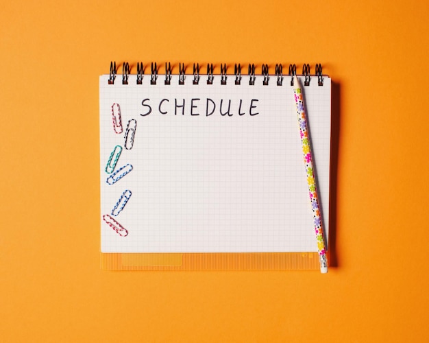 Top view of office tools with blank notebook on orange background