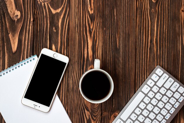 Foto scrittorio di legno dell'ufficio di vista superiore con una tazza di caffè e uno smartphone - copyspace