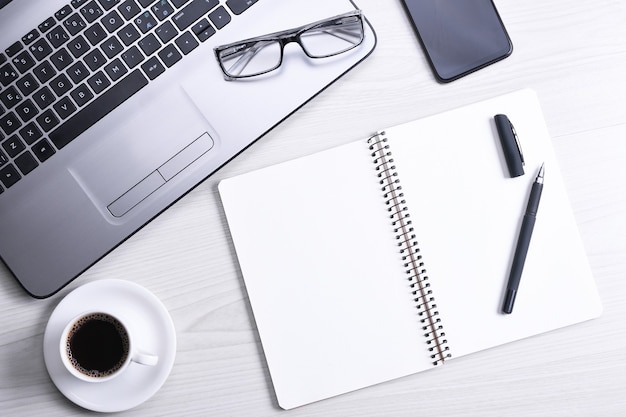 Vista dall'alto dello spazio di lavoro dell'ufficio, tavolo da scrivania in legno con notebook portatile, tastiera, penna, occhiali da vista, telefono, taccuino e tazza di caffè.