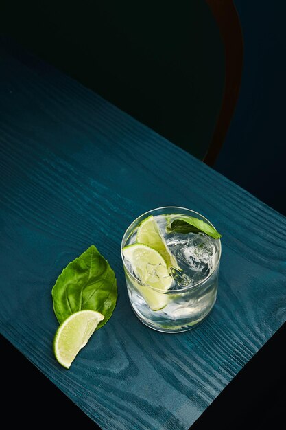 Top view of old fashioned glass with fresh drink mint leaf and lime slice on blue wooden surface