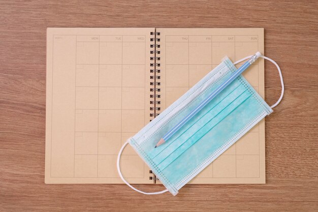 Top view of  old notebooks, anti-virus mask and pencil on wooden table.