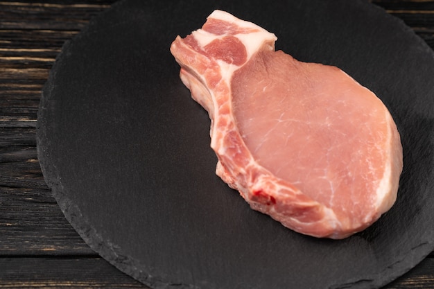 Top view of one pieces raw pork chop steaks on a black stone cutting board.