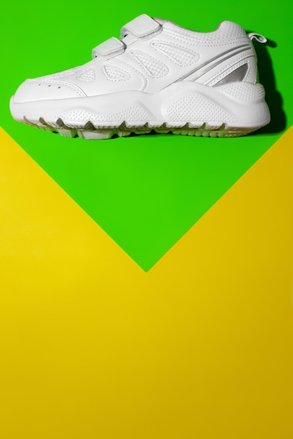 Photo top view one white running shoes on top on a geometric paper green and yellow background with copy s...