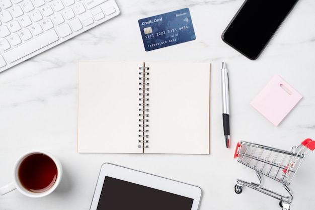 Vista dall'alto del concetto di shopping online con carta di credito ed elettronica isolata sul fondo della tavola bianco marmo ufficio.