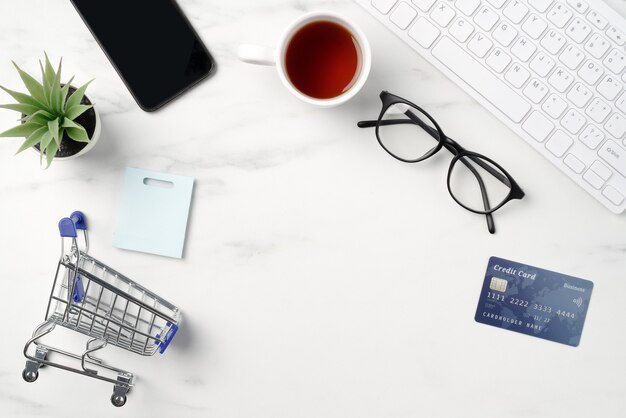 Вид сверху концепции онлайн-покупок с кредитной картой, смартфоном и компьютером, изолированных на фоне офисного мраморного белого стола.