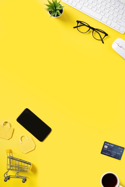 Top view of online shopping concept with credit card, smart phone and computer isolated on office yellow table background.