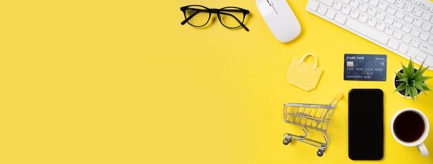 Top view of online shopping concept with credit card, smart phone and computer isolated on office yellow table background.