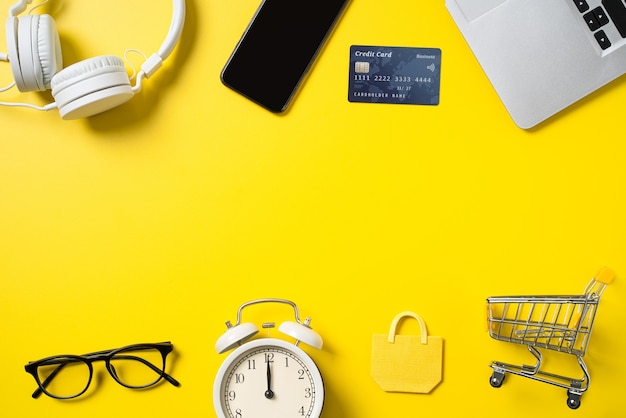 Вид сверху концепции покупок в Интернете с кредитной картой, смартфоном и компьютером, изолированных на фоне желтого стола в офисе.