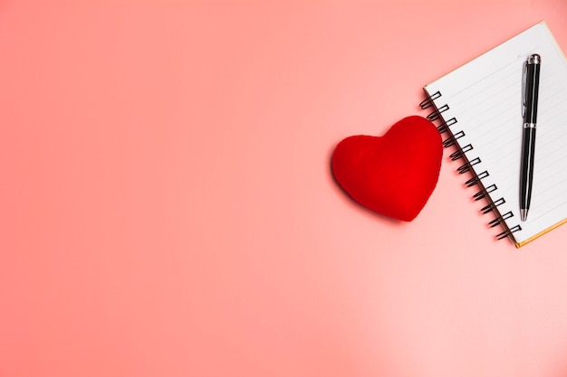 Top view of open book red heart. Book open with pen on pink background.