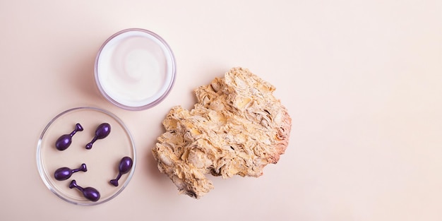 Top view of open box with white cream and cosmetics capsules in petri dish near it