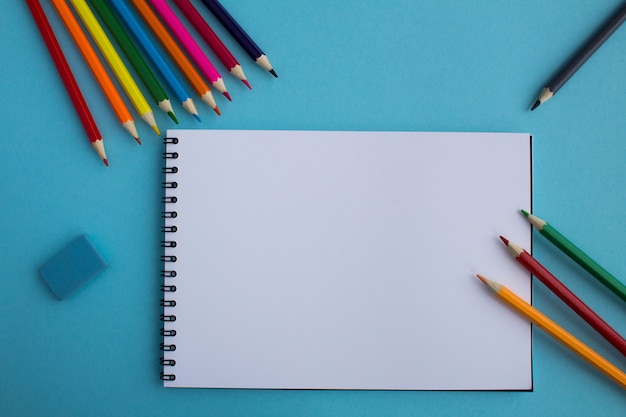 Top view of an open notepad and color pencils on the blue surface.Copy space.