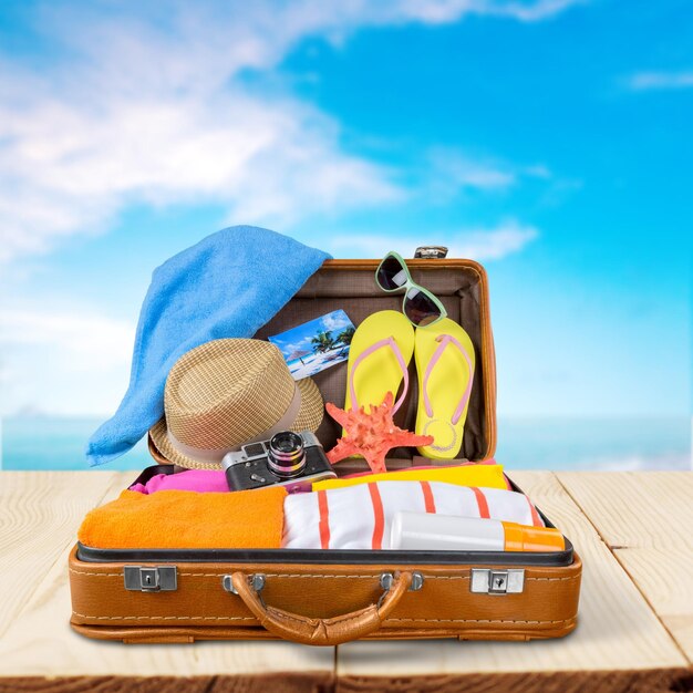 top view of an open suitcase with full of summer stuff on blue background