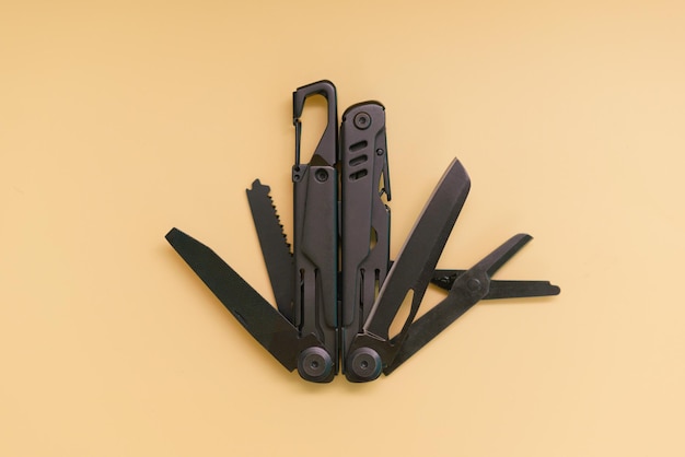 A top view of opened black multitool device stands on a yellow background Scissors a saw blade a screwdriver attachment an opener and a knife Multitool Universal Folding Screw Metallic