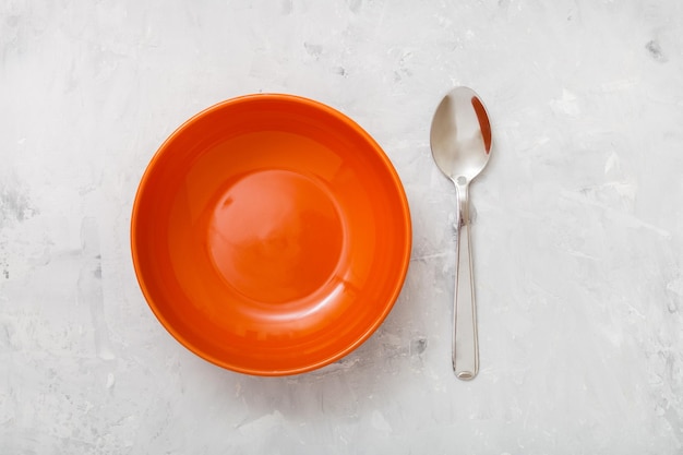 Top view orange bowl and spoon on concrete plate