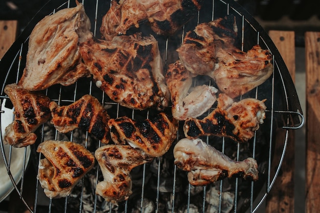 Top view of overcooked chicken breast and wings on a grill outdoors