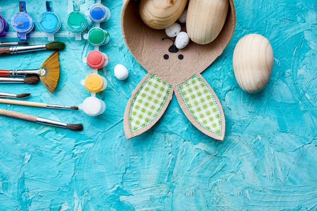 Top view pack of eggs with brush, paint and decorative elements on blue background. Copy space, Happy Easter, DIY, flat lay.