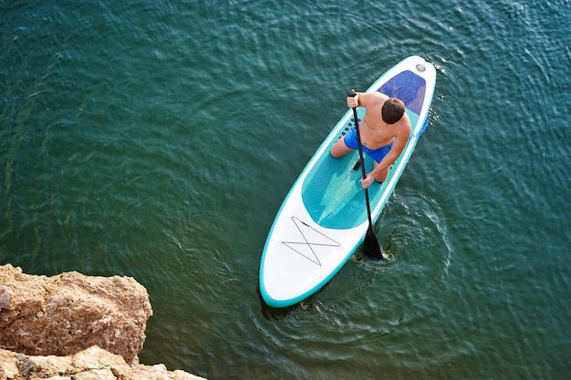 Top view on paddleboard sup man having fun paddle board fitness\
recreational leisure activity beach rental equipment on travel\
vacation