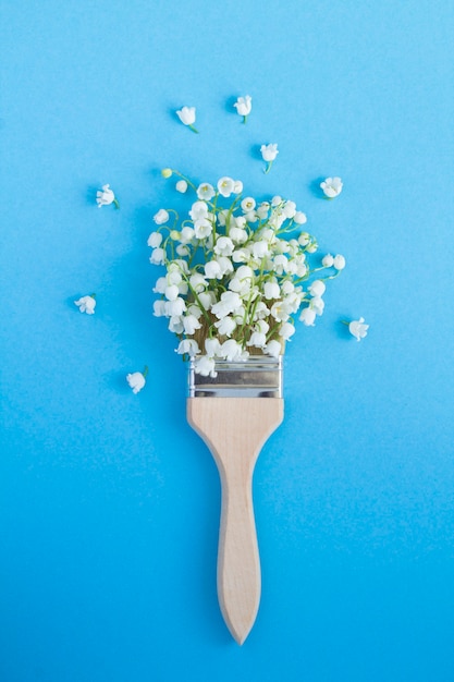 Top view of paintbrush with lilies of the valley on the blue background