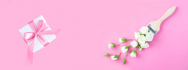 Top view of paintbrush with white rose and gift box on the pink background Copy space Banner