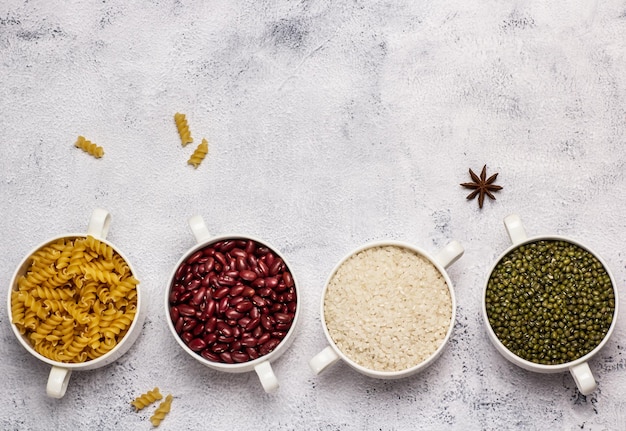 Top view of pasta kidney beans rice and mung beans in bowls on white concrete background