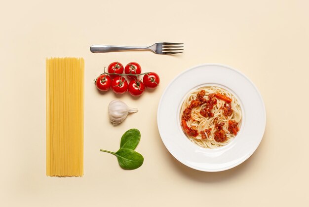 Top view of pasta with meat near tomato garlic basil leaves and fork on beige background