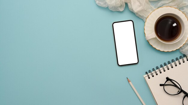 Фото Вид сверху пастельный синий фон с копировальным пространством, макет белого экрана смартфона и аксессуары