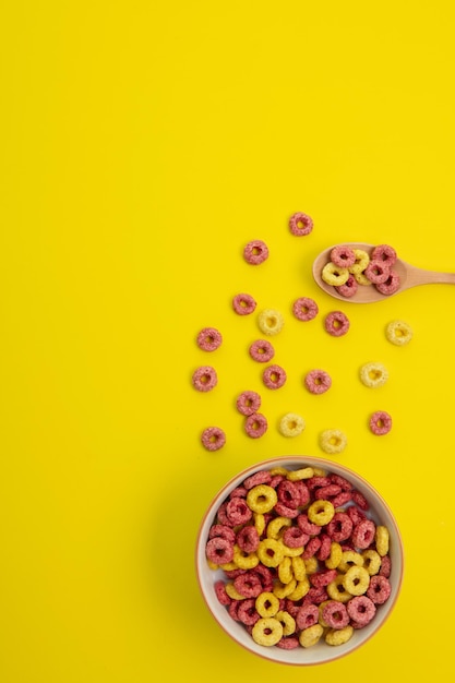 Top view of pattern of cereals with spoonful of cereal and bowl of cereal on yellow background