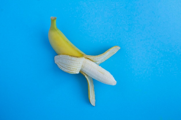 Top view of on peeled banana on the blue background Copy space