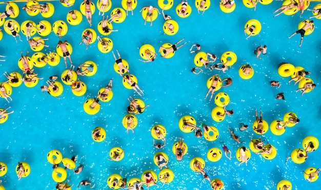 Foto vista dall'alto di persone che si rilassano in piscina su cerchi gonfiabili gialli.