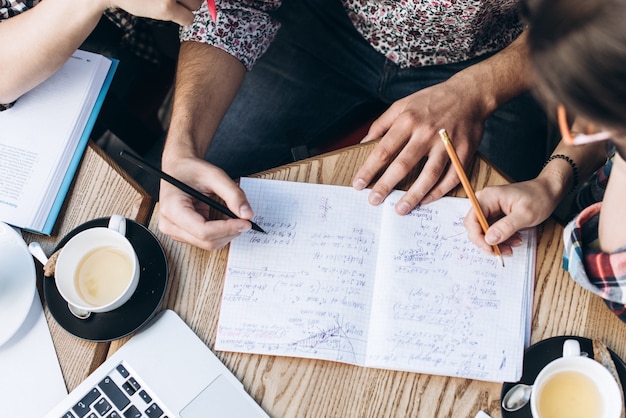 Vista dall'alto delle persone che studiano con il libro di libro, il libro e il computer portatile. tazze di caffè sul tavolo