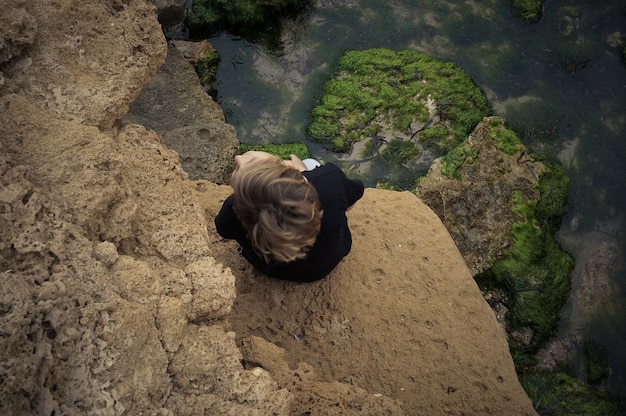 Photo top view to a person sitting on rocky beach