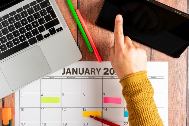 Top view of person touching digital tablet next to calendar of the month Colored adhesive note