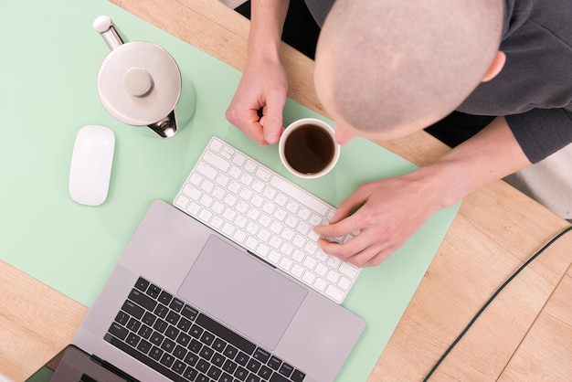 Top view photo of a bald man working on the laptop and drinking\
tea on a table creativity designer development employment gadget\
inspiration job learning teapot concept internet online