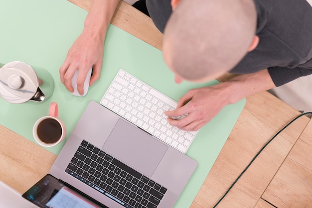 Top view photo of a bald man working on the laptop on a wooden\
table with a big green pad distant online minimal keyboard\
organization remote working wireless planning