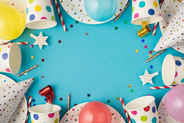 Top view photo of birthday party table composition candles pipes striped straws hats sequins balloons polka dots paper cups and plates on isolated blue background with copyspace