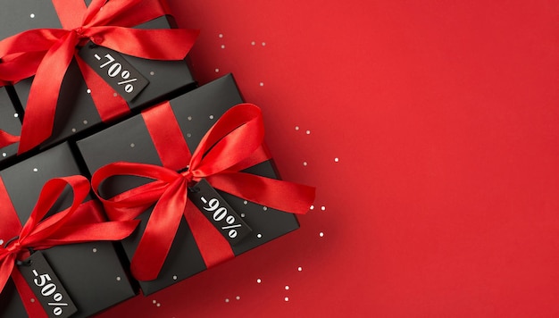 Top view photo of black gift boxes with red ribbon bow and confetti on isolated red background with text on price tag