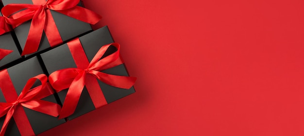 Вид сверху фото черных подарочных коробок с красной лентой на изолированном красном фоне с копирайтом