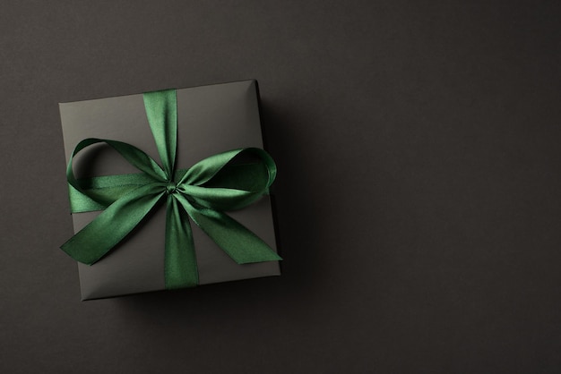 빈 공간이 있는 격리된 검은색 배경에 녹색 리본 활이 있는 검은색 선물 상자의 상위 뷰 사진