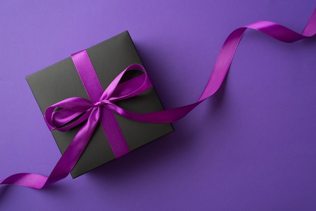 Top view photo of black giftbox with purple ribbon bow on isolated violet background with empty space