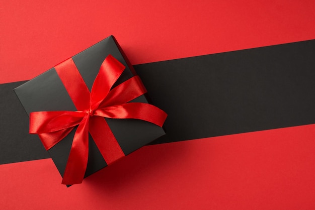 Top view photo of black giftbox with vivid red ribbon bow on isolated two color red and black background with copyspace