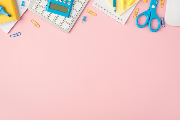 파란색 및 노란색 편지지 주최자 연필 마커 클립 핀 가위 스티커 계산기 키보드 마우스의 위쪽 보기 사진은 카피스페이스가 있는 격리된 파스텔 분홍색 배경에 있습니다.