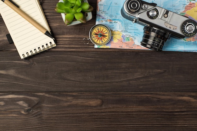 Photo top view photo of camera and compass on map notebook pen plant on isolated wooden table background with copyspace