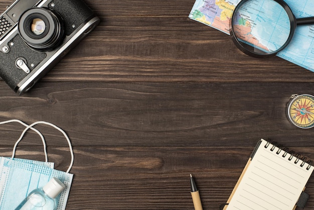 Foto foto vista dall'alto della mappa della fotocamera lente d'ingrandimento bussola penna notebook maschere mediche e disinfettante su sfondo tavolo di legno isolato con copyspace al centro